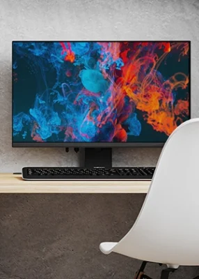 Veliki kompjuterski monitor sa šarenom pozadinom na ekranu stoji na stolu ispred koga je bela stolica